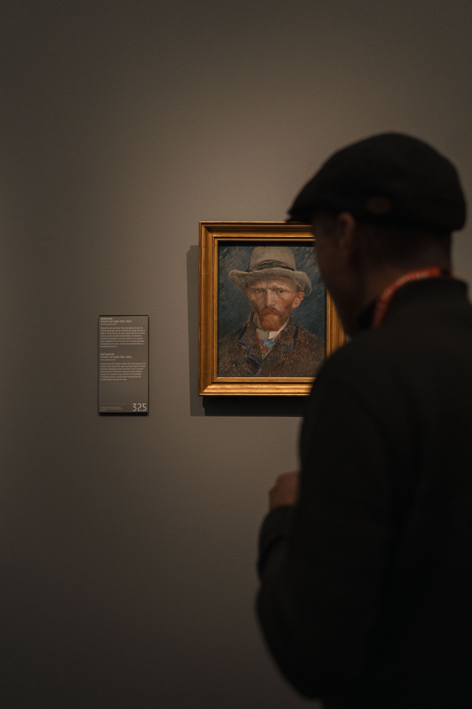 Visitor viewing a framed portrait in a dim museum gallery with a wall label nearby