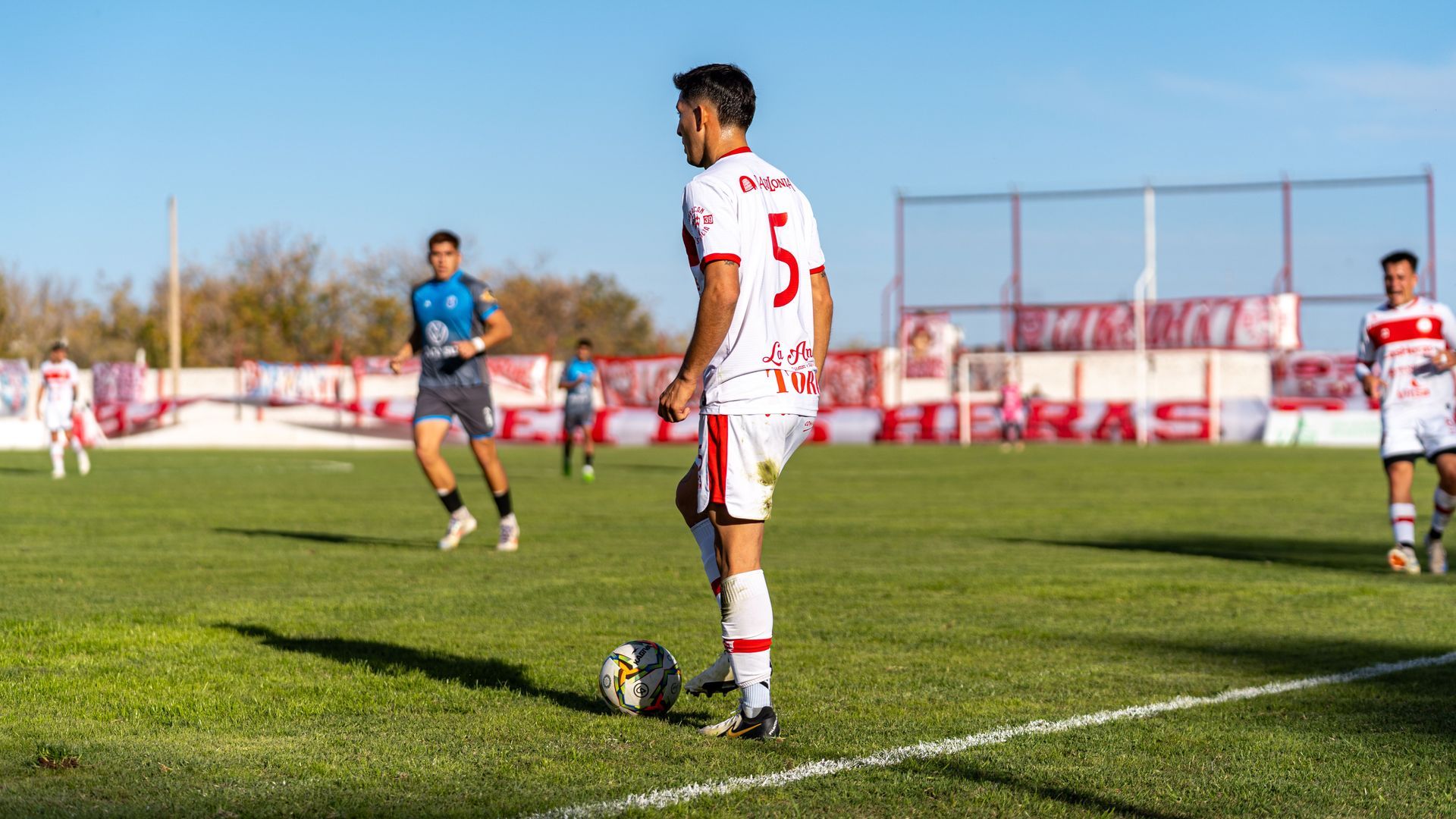 Soccer player in white jersey prepares to kick the ball on a sunny field during a match