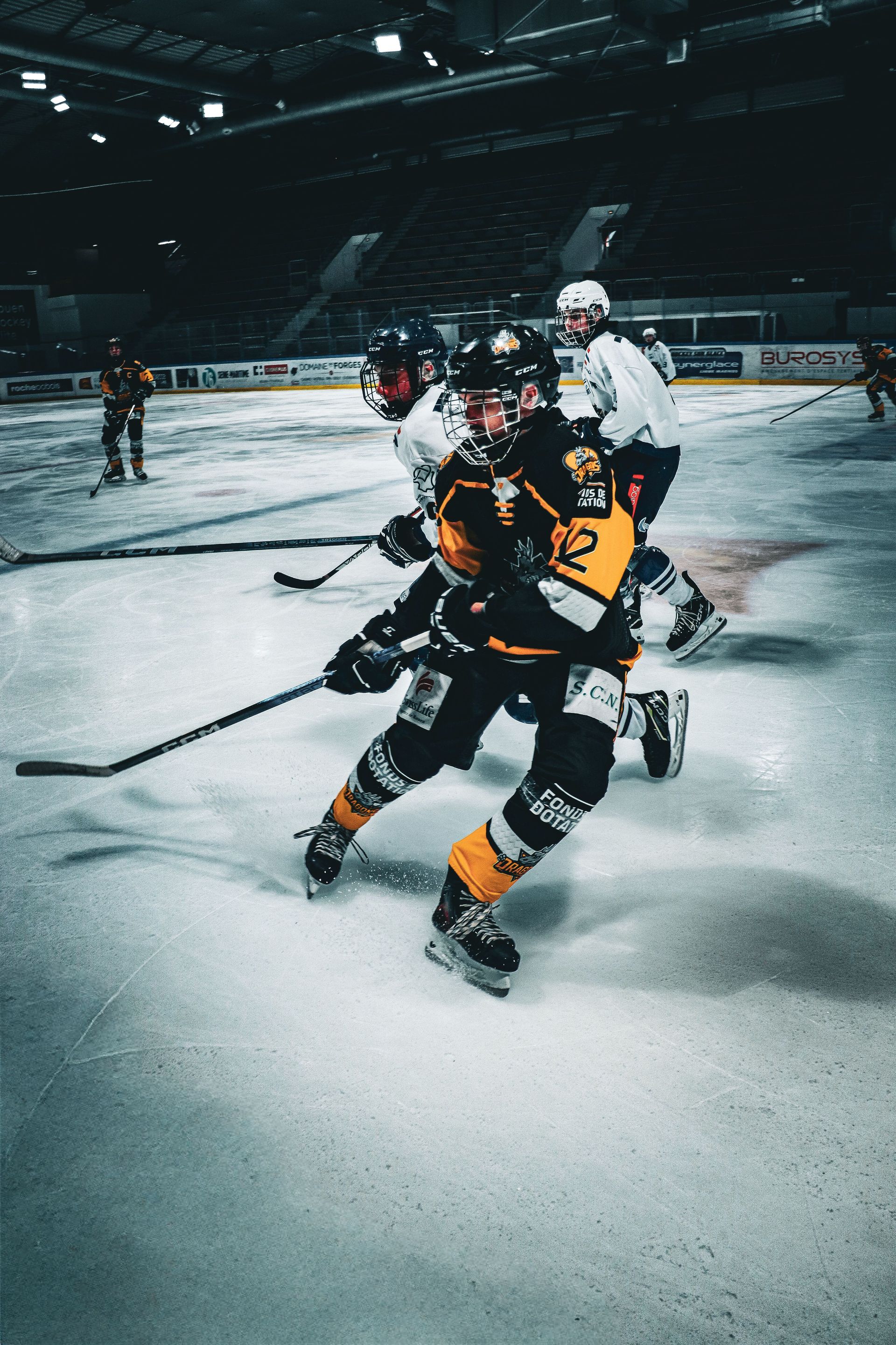 Ice hockey player in black and yellow skates hard on an indoor rink, with opponents behind him.
