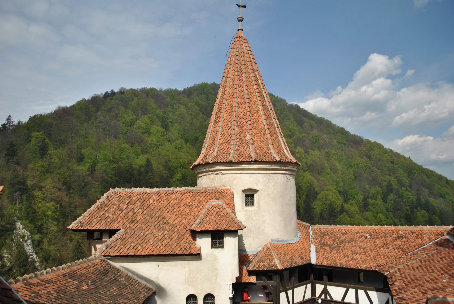 Stone church with a red-tiled tower roof against green hills and a cloudy sky