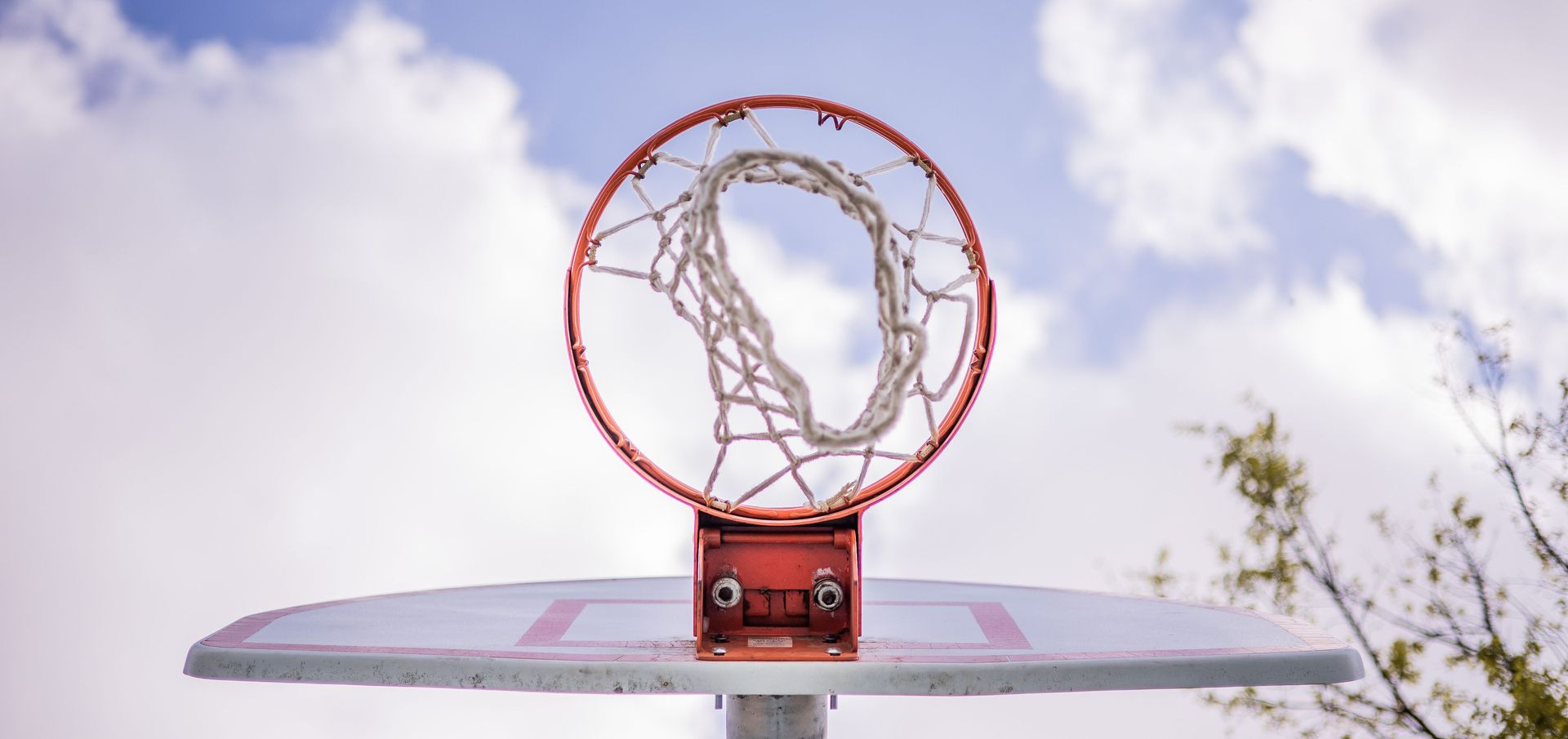 Red basketball hoop with a bent net on an outdoor table against a cloudy sky