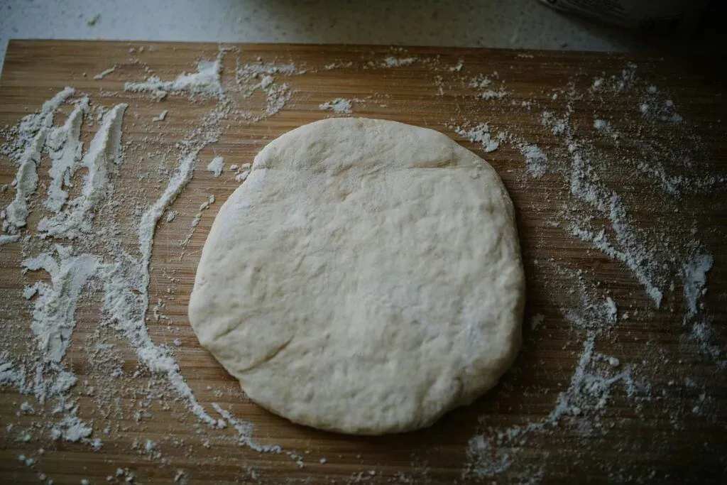 Floured wooden board with a round ball of dough in the center