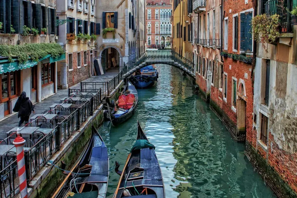 Venice canal with gondolas, red-brick buildings, and a stone bridge over green water