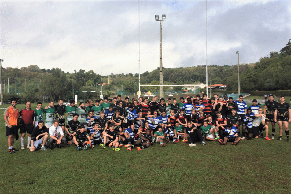 Large group of athletes and coaches posing on a grassy sports field with goalposts and trees in the background