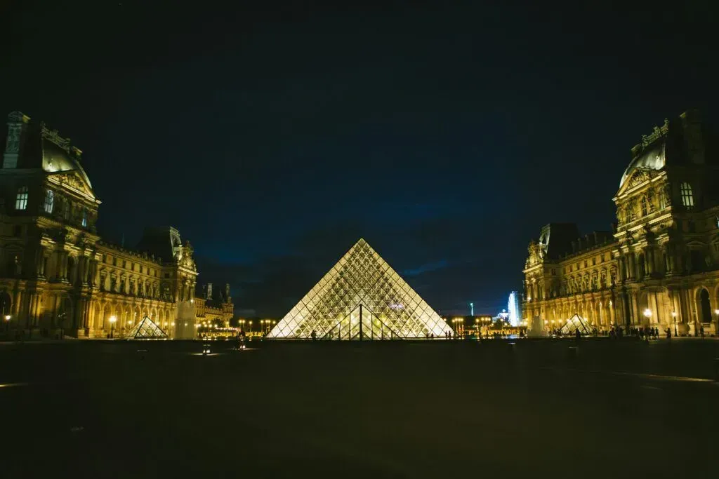 Night view of the Louvre Pyramid lit gold, centered between illuminated museum wings