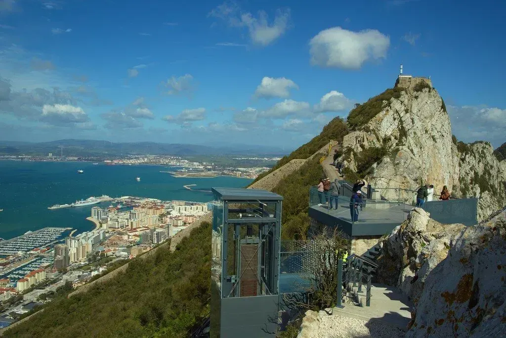 Rocky cliff viewpoint overlooking a coastal city and blue sea under a bright sky