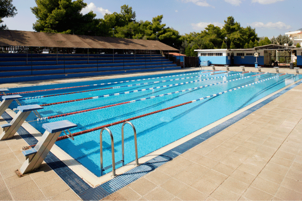 Outdoor swimming pool with blue lanes, diving blocks, and shaded seating area