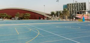 Blue outdoor sports court beside a red building and bleachers under a clear sky