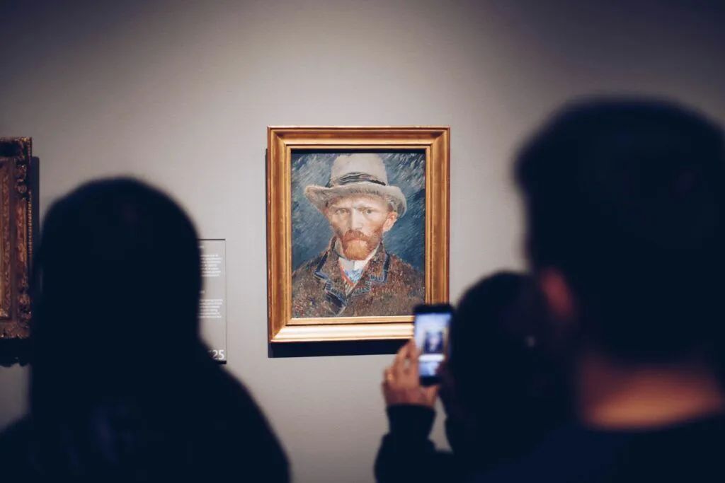 Museum visitors photograph a framed portrait on a gallery wall.