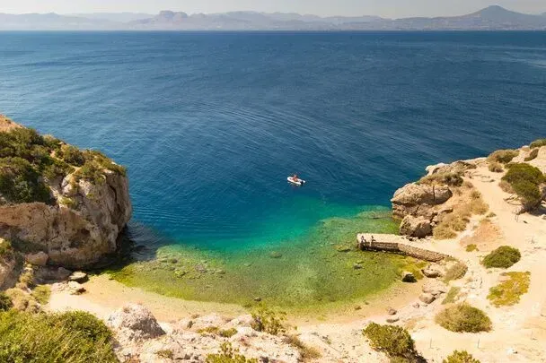 Rocky cove with turquoise water, sandy shore, and a small boat in the distance
