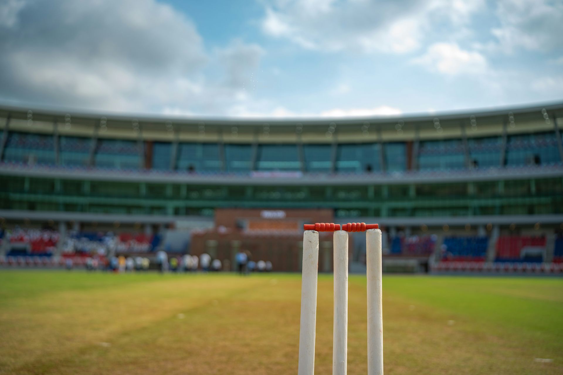 A cricket wicket in focus and a blurred cricket stadium behind it as the background 