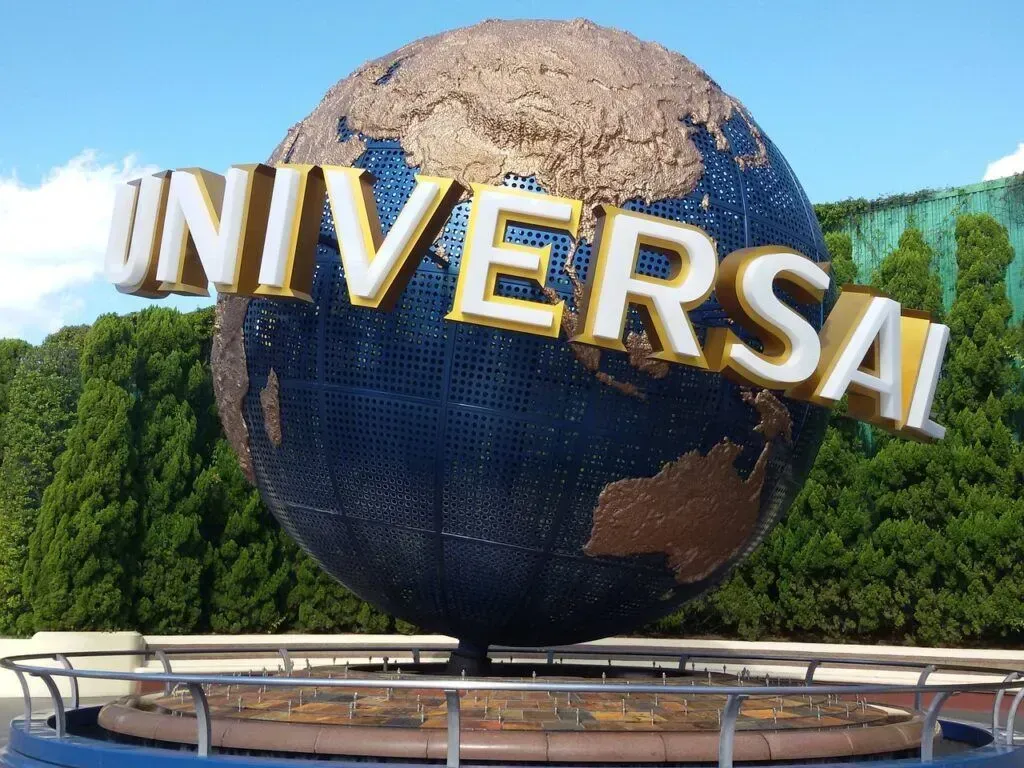Universal Studios globe sign with gold letters in front of green trees and blue sky