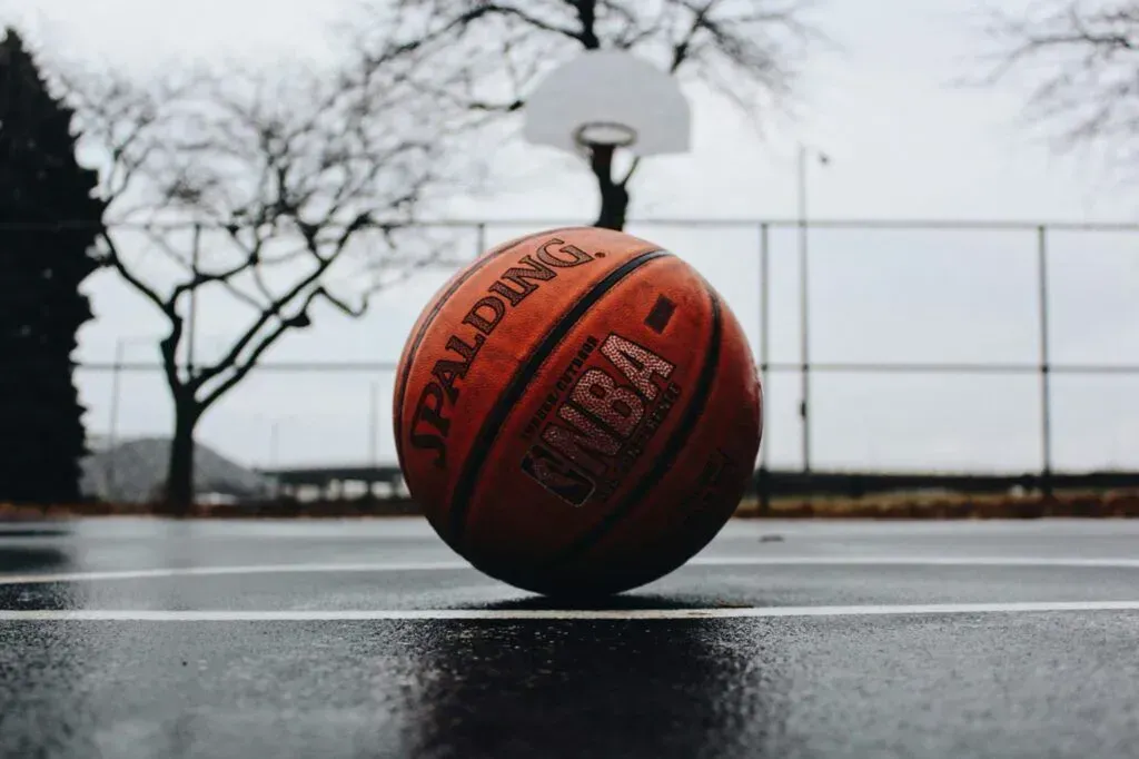 Orange basketball on a wet outdoor court with a hoop in the background