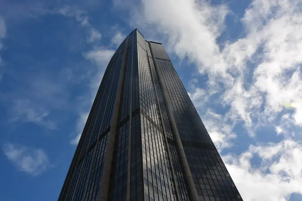 Tall glass skyscraper shot from below against a blue sky with clouds