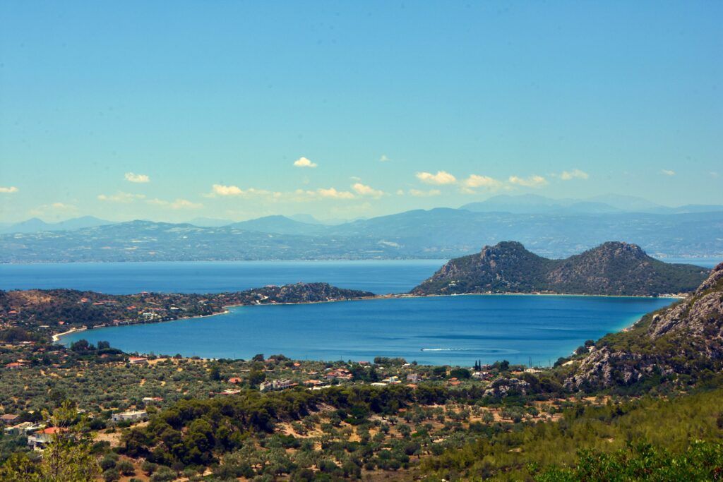 Blue lake bay with distant mountains, green hills, and a clear sky