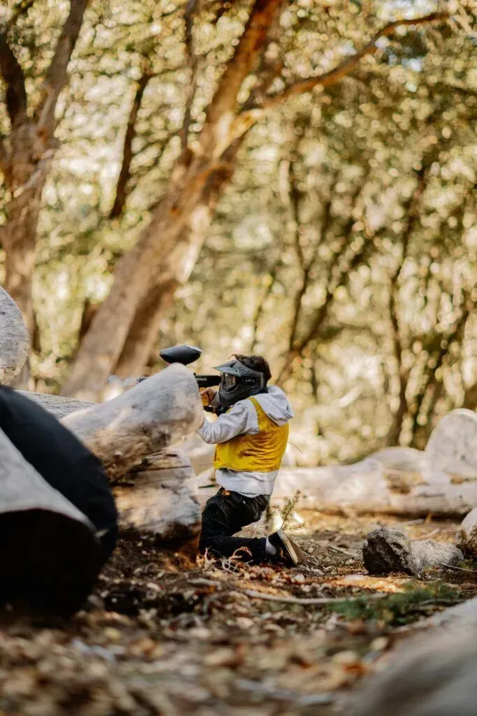 Person in a yellow shirt sitting outdoors among trees and fallen logs, surrounded by leaves.