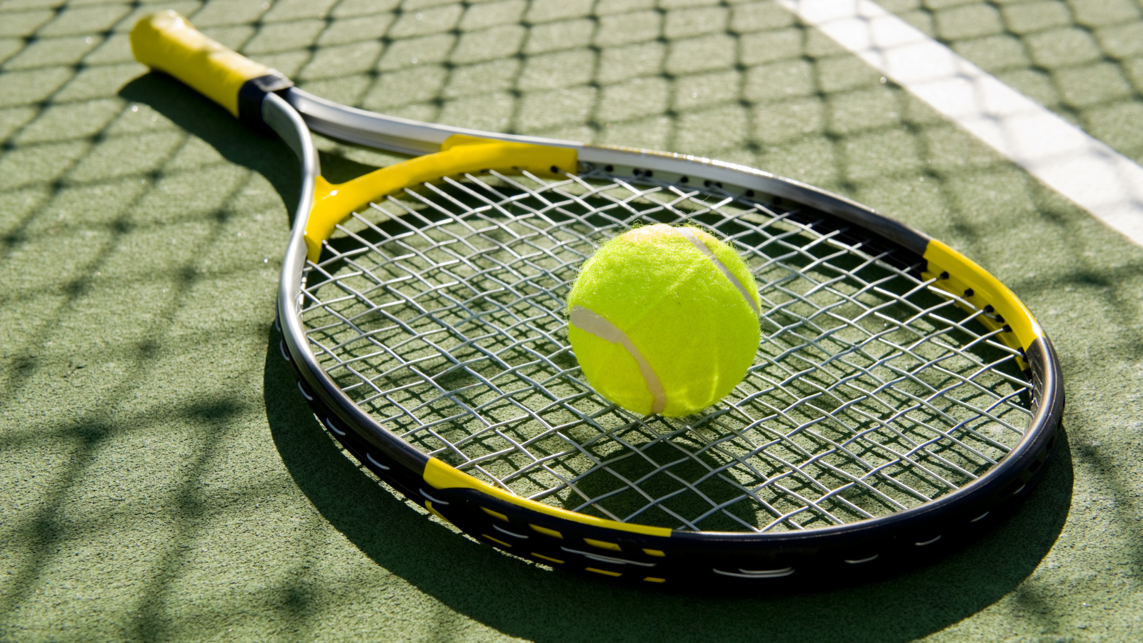Tennis racket with a tennis ball on a hard court
