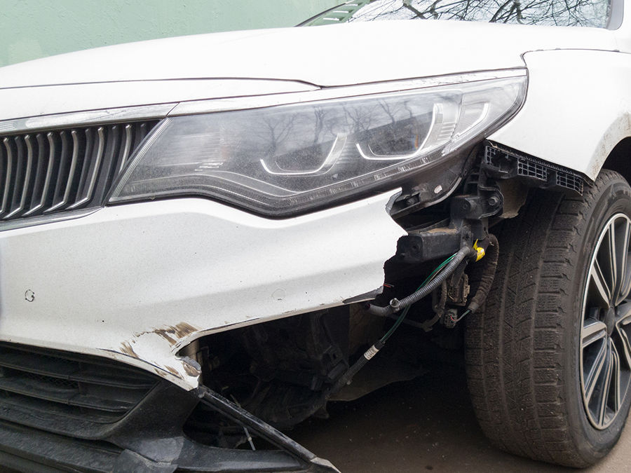 A white car with a damaged front bumper is parked on the side of the road.