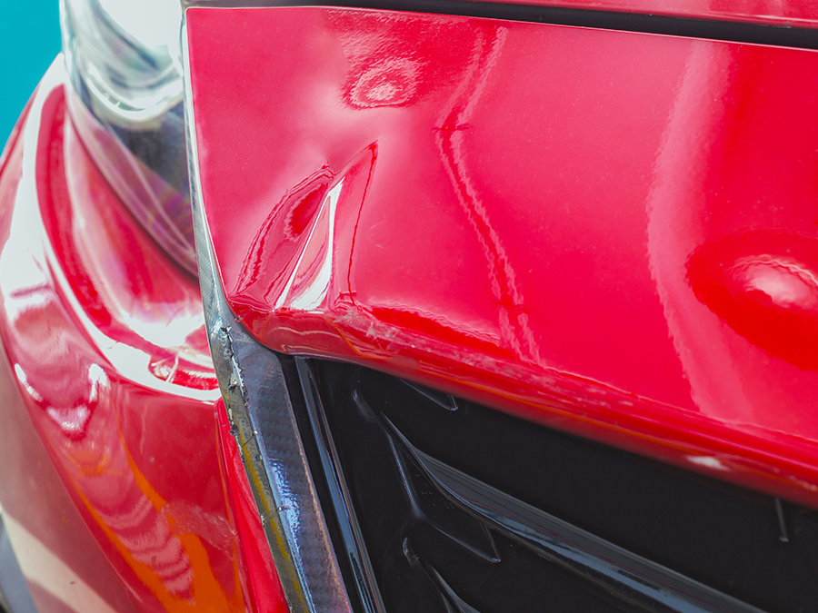 A close up of a red car with a damaged bumper.