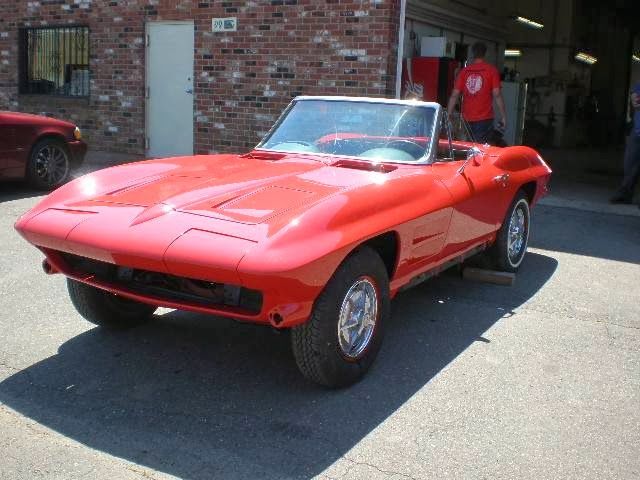 A red corvette convertible is parked in front of a brick building
