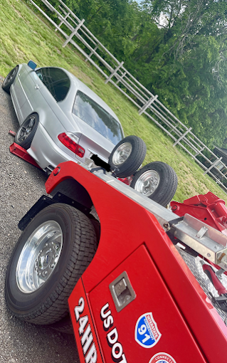 A silver car is being towed by a red tow truck.