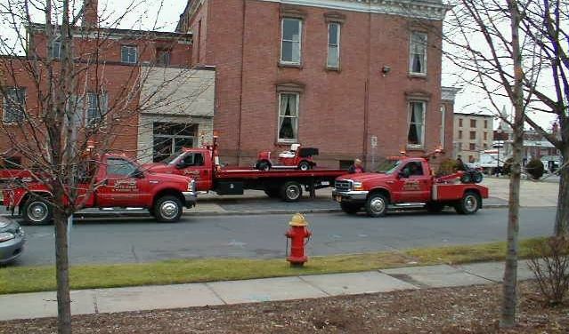 Two red tow trucks are parked in front of a brick building