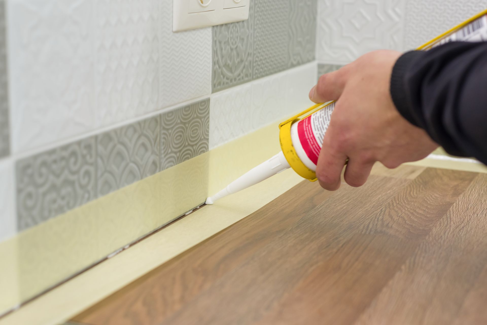 A person is applying silicone sealant to a wooden floor.