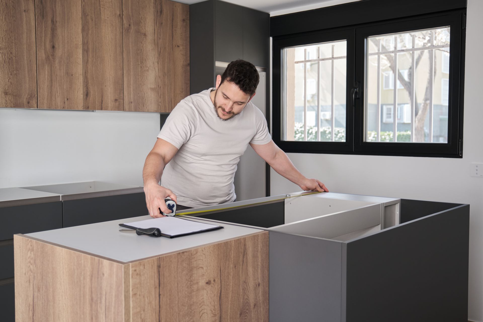 A man is measuring a kitchen counter with a tape measure.