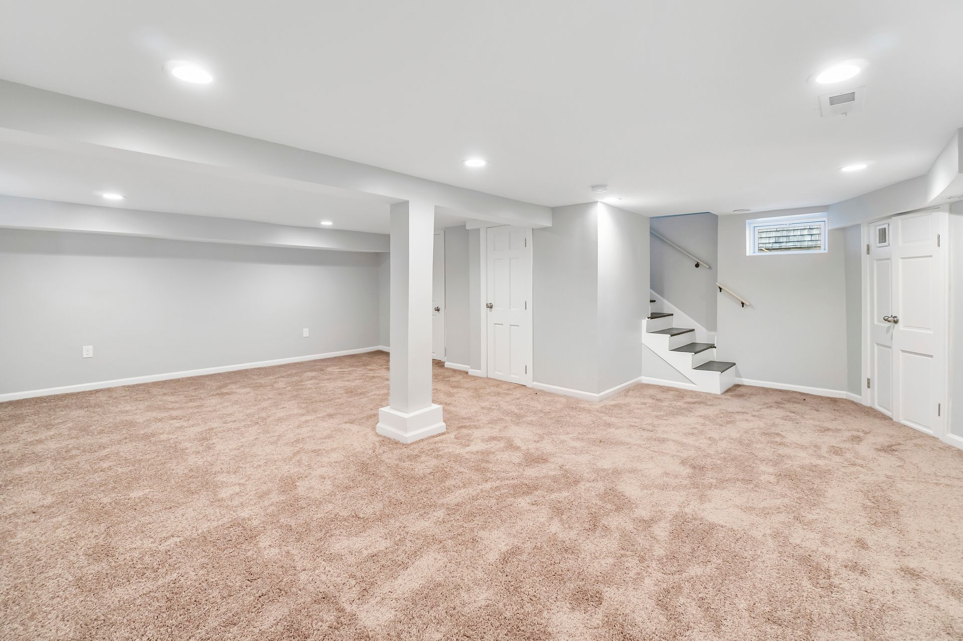 An empty basement with carpeted floors and white walls.