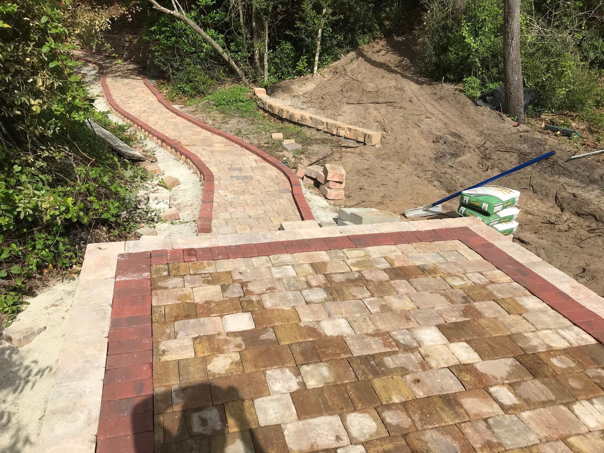 Curving brick walkway leading up a dirt slope beside a wooded area
