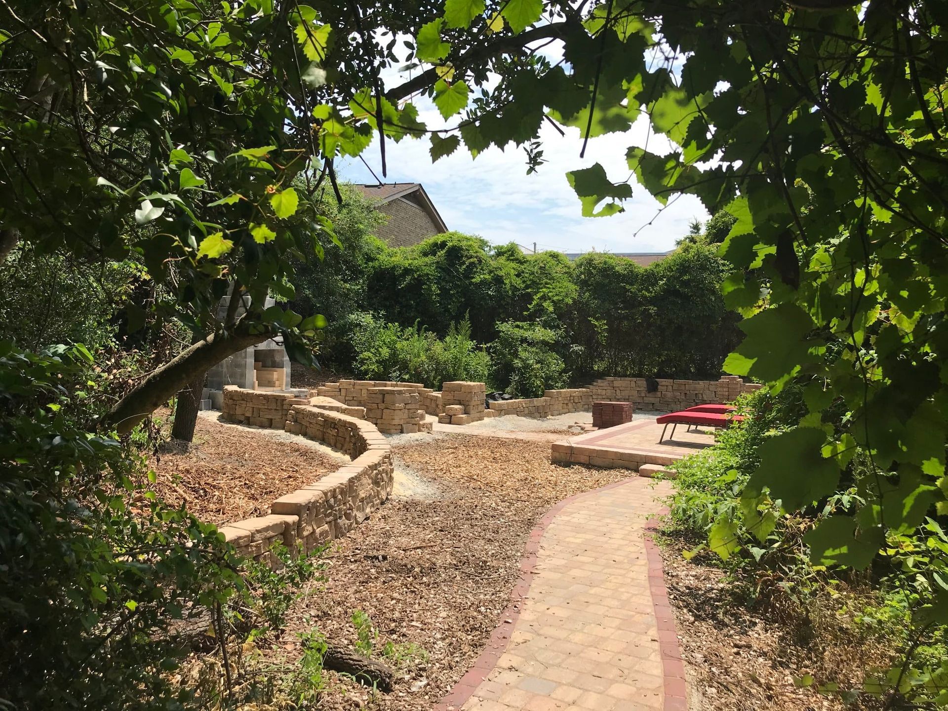 Stone patio garden with a winding path, leafy archway, and outdoor seating in the distance