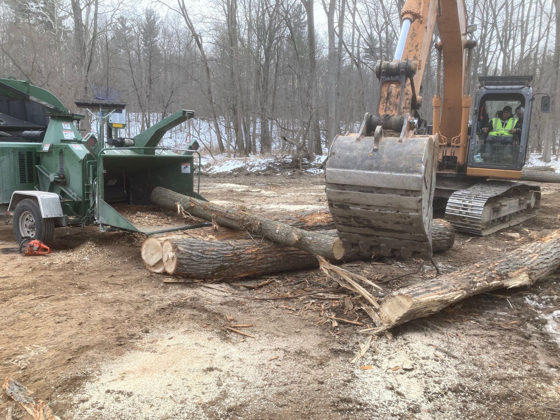 Excavator and wood chipper processing logs in a snowy forest clearing