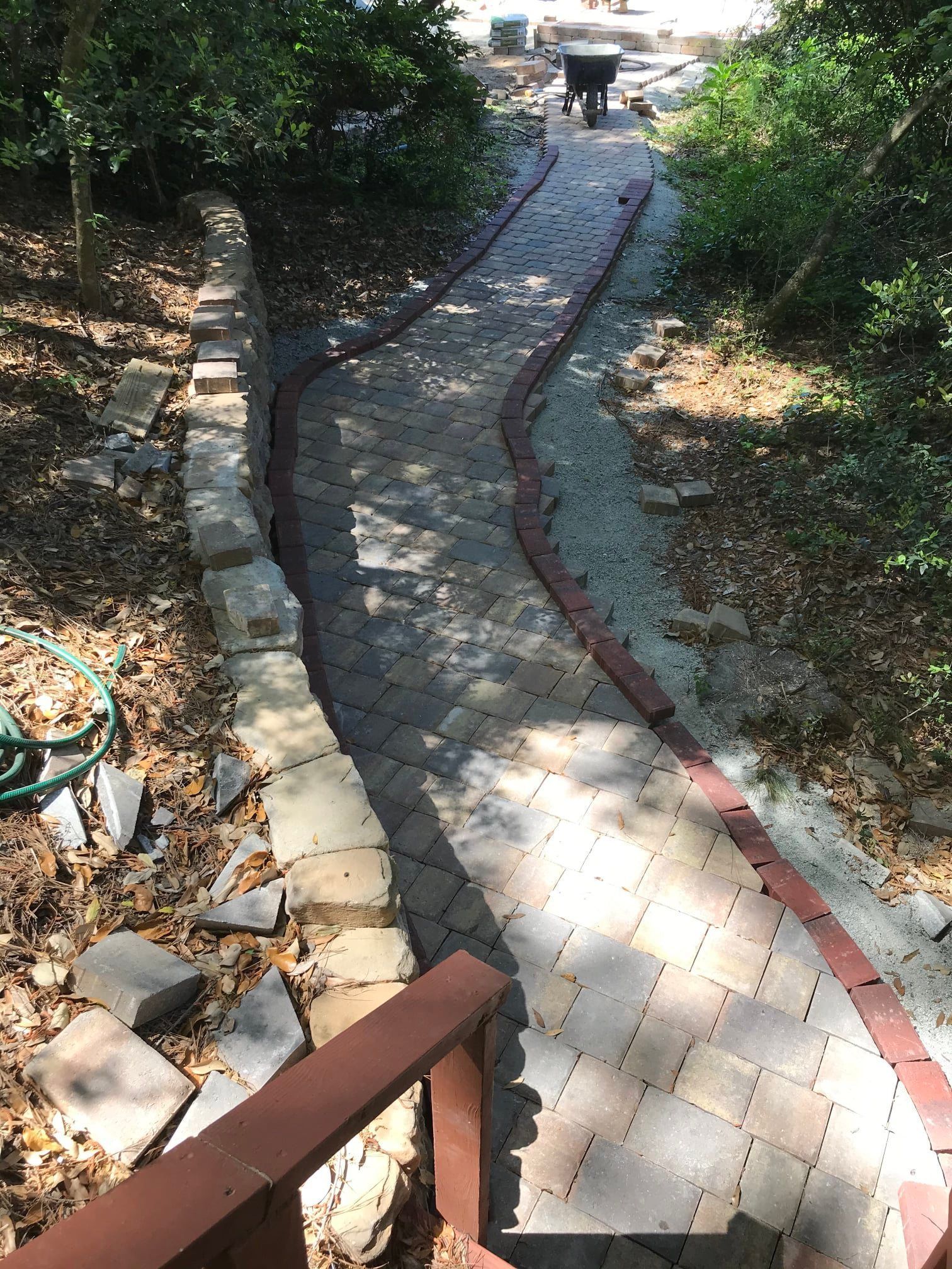 Curved brick walkway on a slope with red border, bordered by rocks and trees in a garden area
