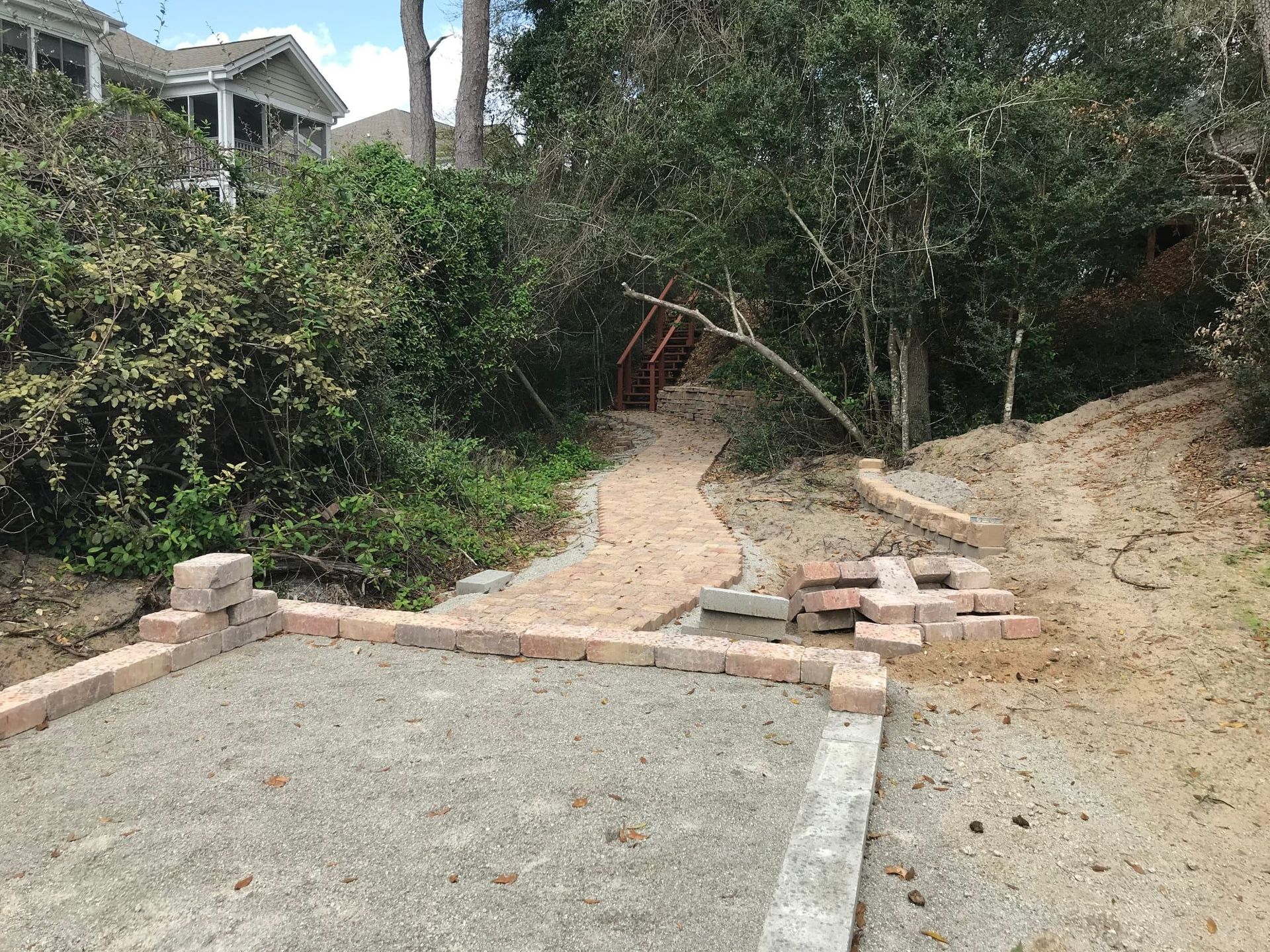 Backyard path leading up a dirt slope beside shrubs and trees, with a concrete slab in the foreground