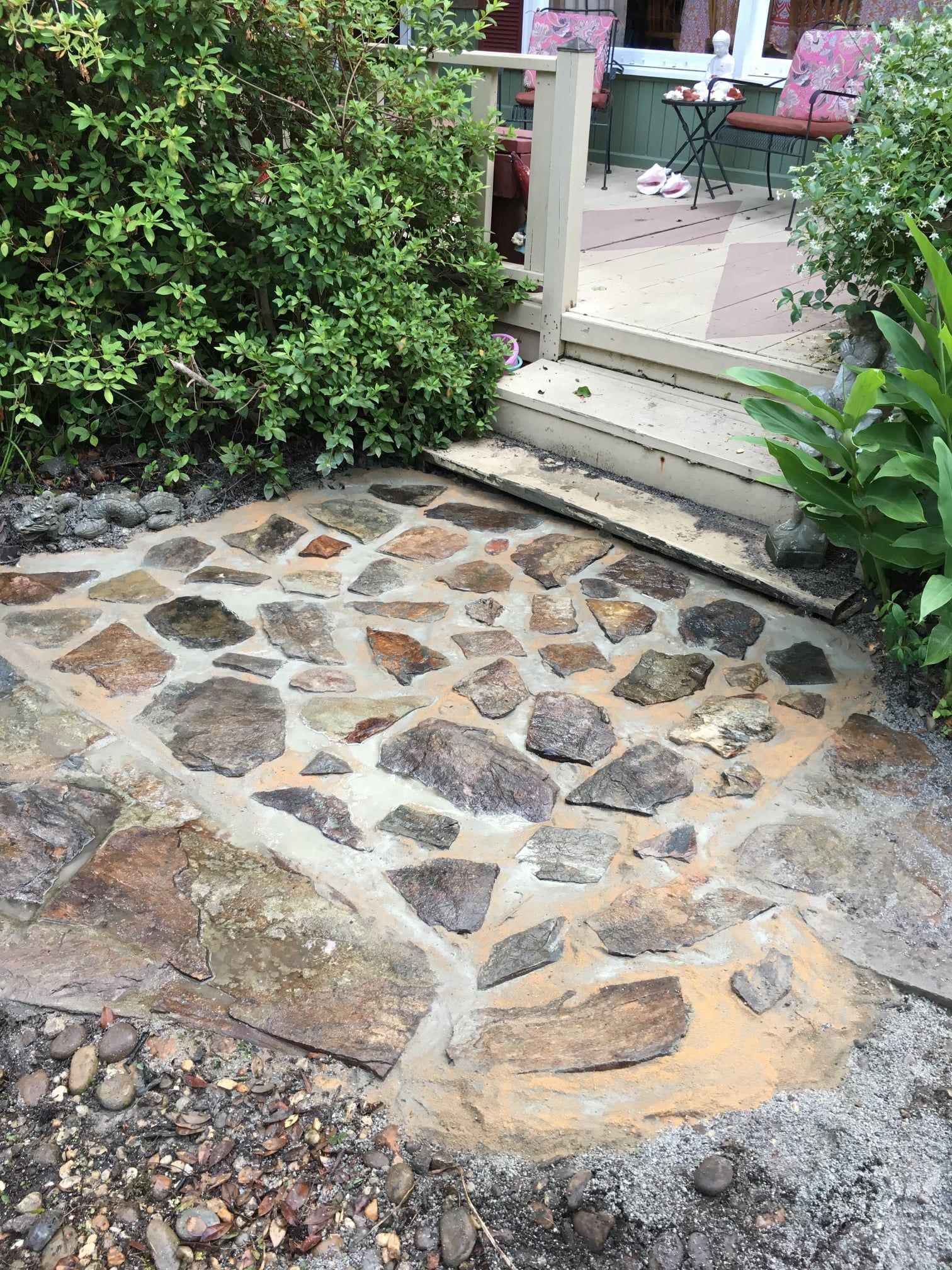 Stone-paved garden path leading to a porch with steps and lush greenery nearby