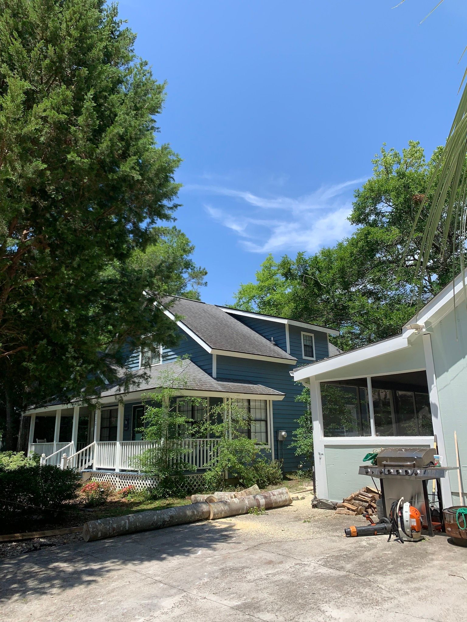 Sunny backyard courtyard with white house, patio chairs, trees, and a grill under a blue sky