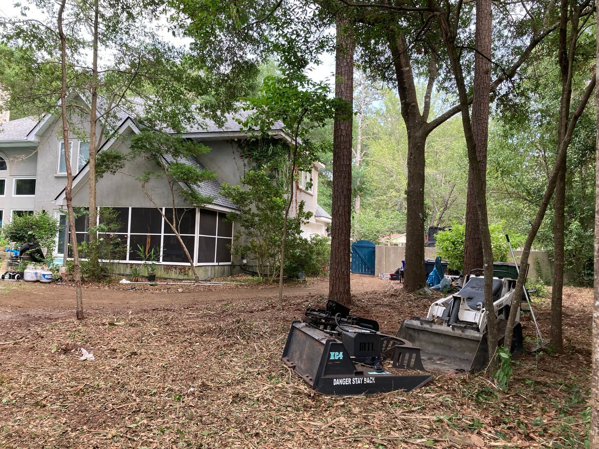 Leaf-covered yard with trees, a house in the background, and construction debris in the foreground
