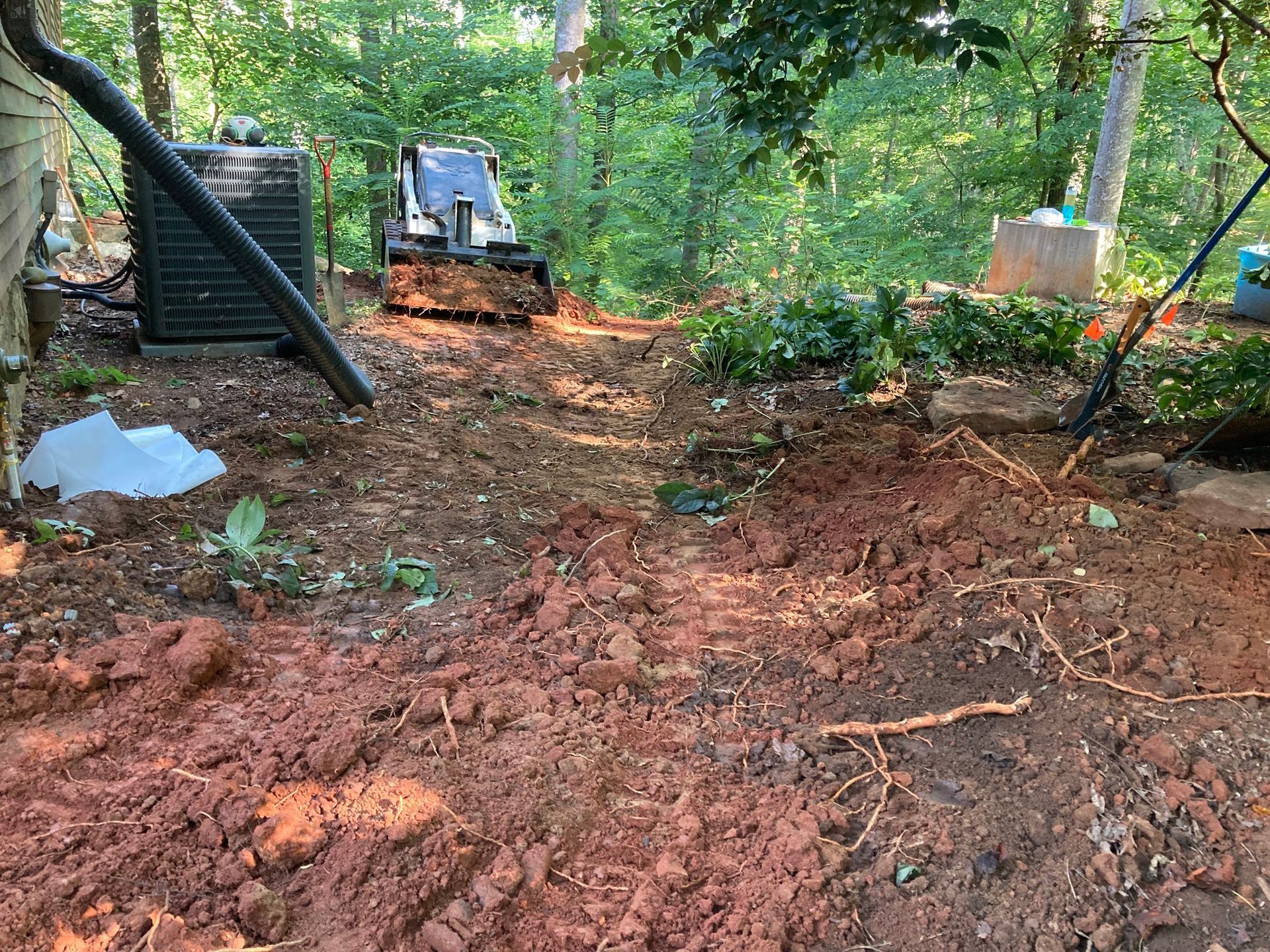 Cleared dirt path through a wooded yard with construction equipment and scattered debris