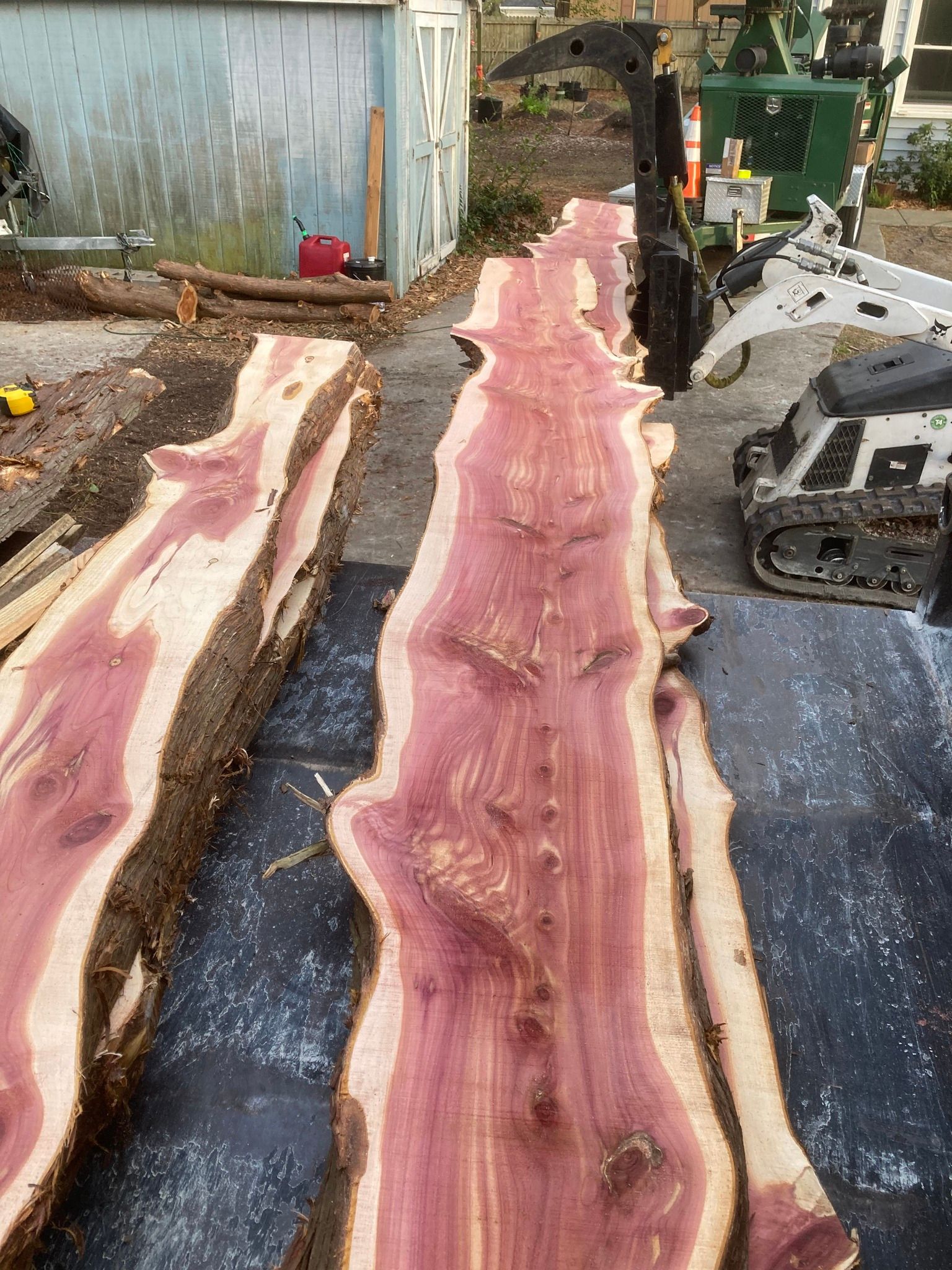 Two long, pinkish wood slabs laid on a work surface in an outdoor workshop.