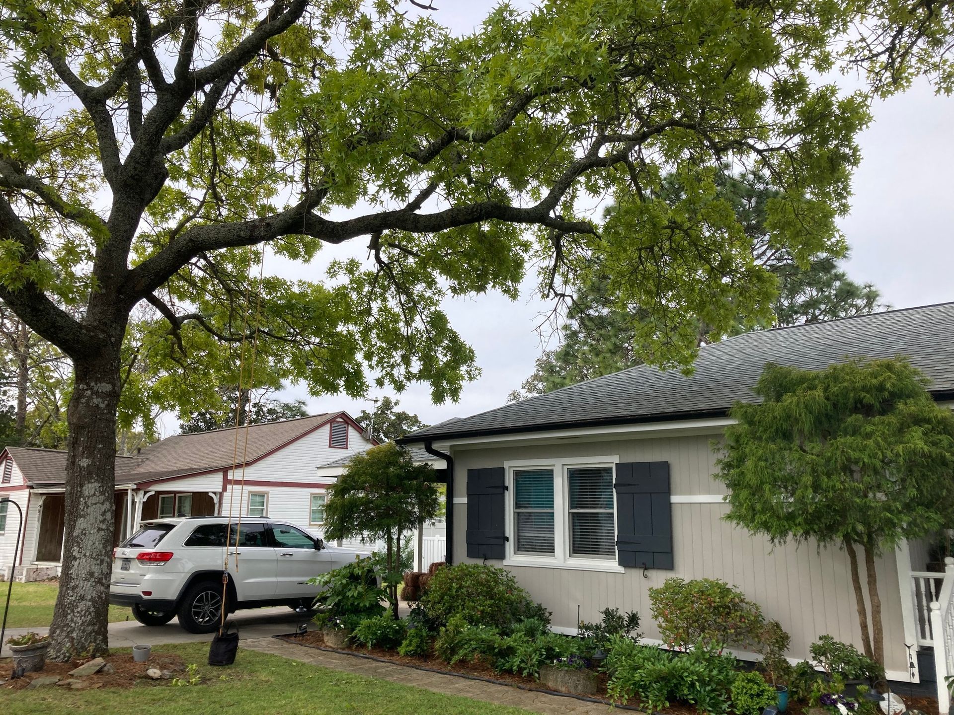 Suburban street with trees, a gray house, and a white SUV parked in the driveway.