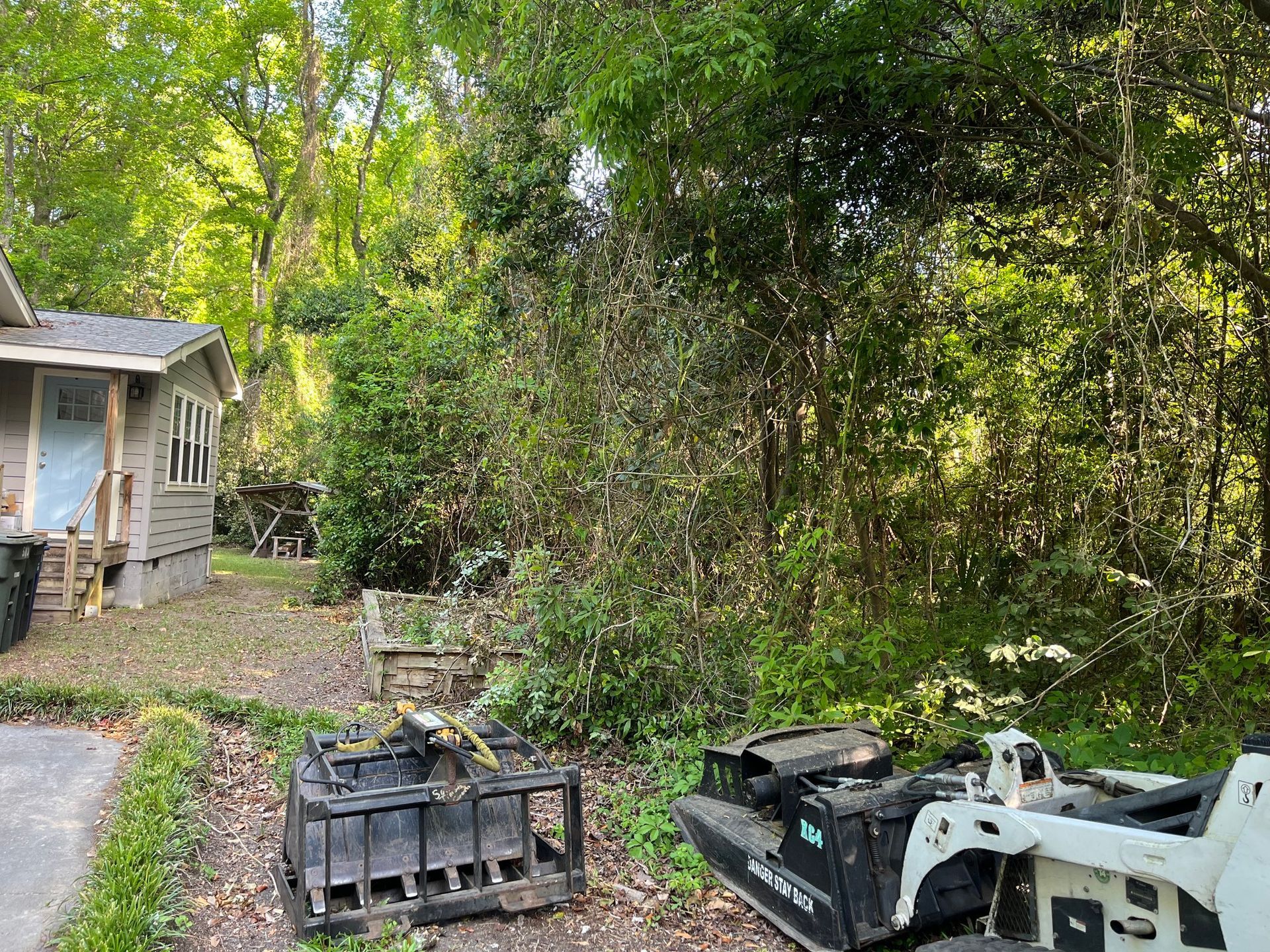 Backyard with trees, gravel path, a shed, and a white skid steer beside stacked pallets.
