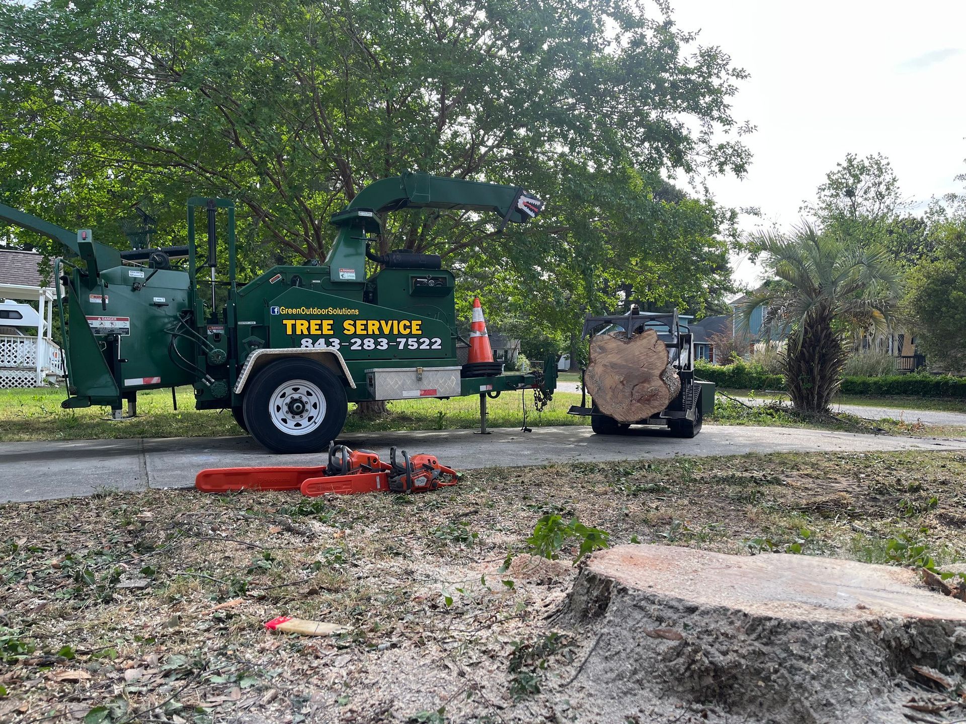 Tree service truck with lifted bucket parked beside a tree in a yard, with cut branches on the ground.