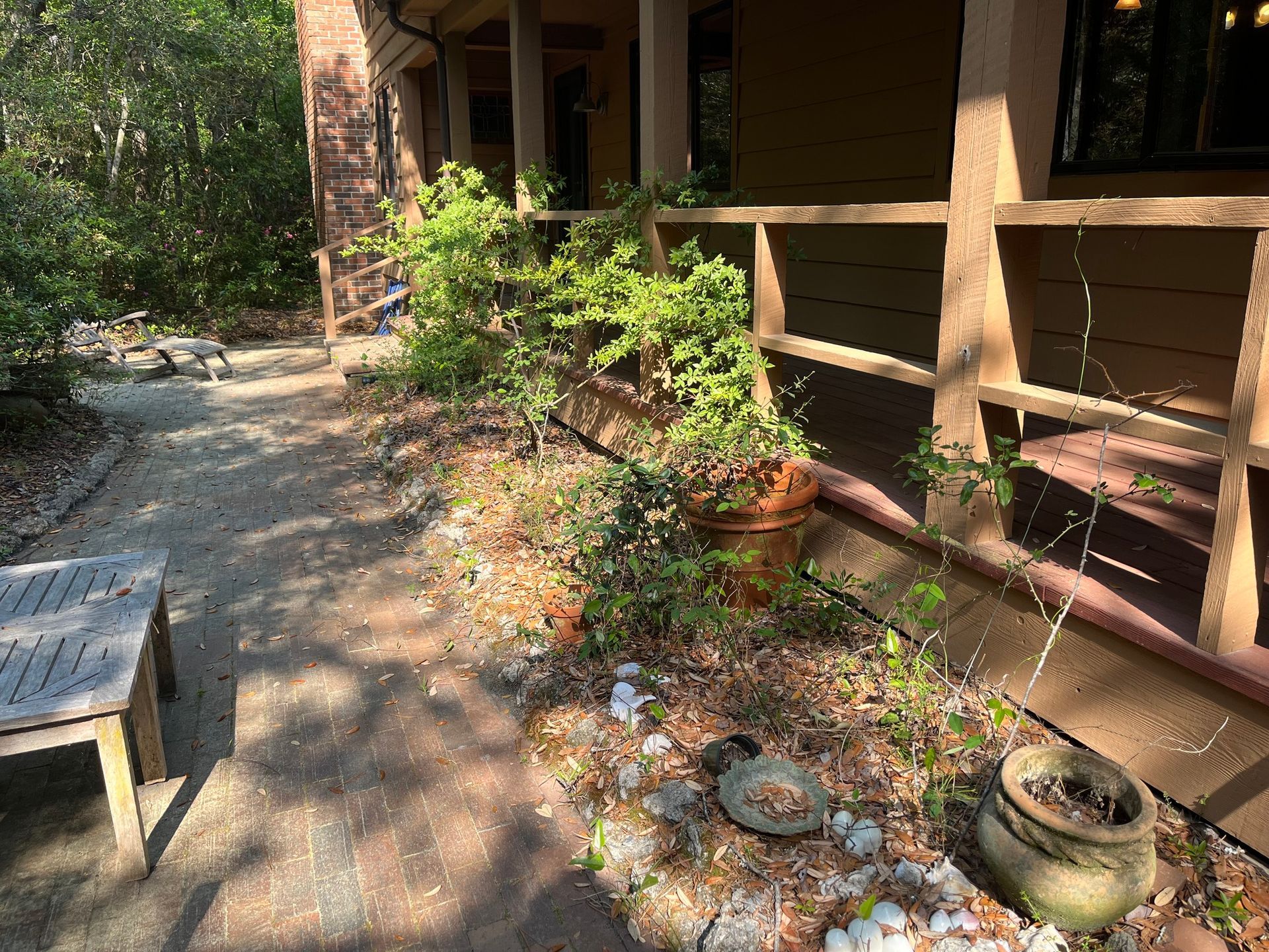 Shaded garden walkway beside a rustic building, with potted plants and stone planters along the path