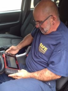 Man in blue shirt using a diagnostic tool inside a car.