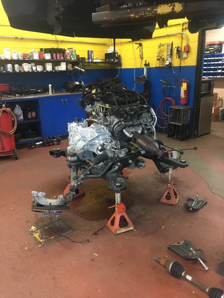 Black car on a red lift in a garage, being worked on; alignment equipment attached to wheels.