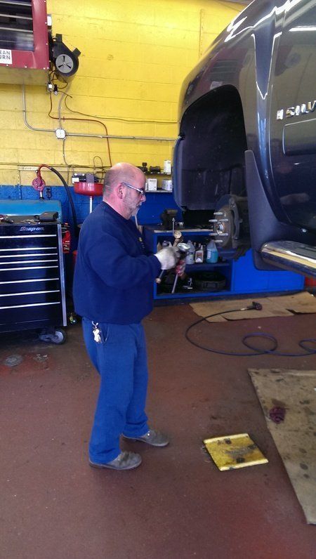 Mechanic working on vehicle lifted in a garage, wearing blue coveralls.