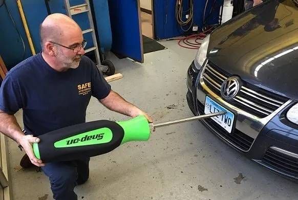 Man kneeling with a large Snap-on screwdriver, appearing to unscrew a car's license plate.