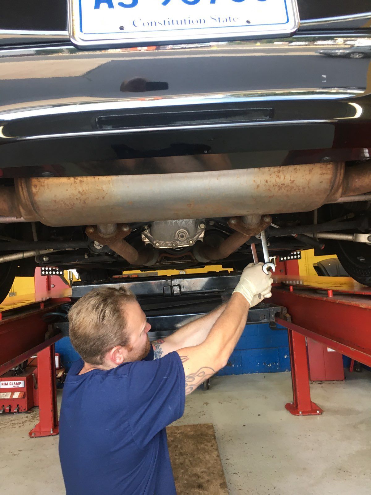 Mechanic under a car, using a wrench to work on the exhaust system.