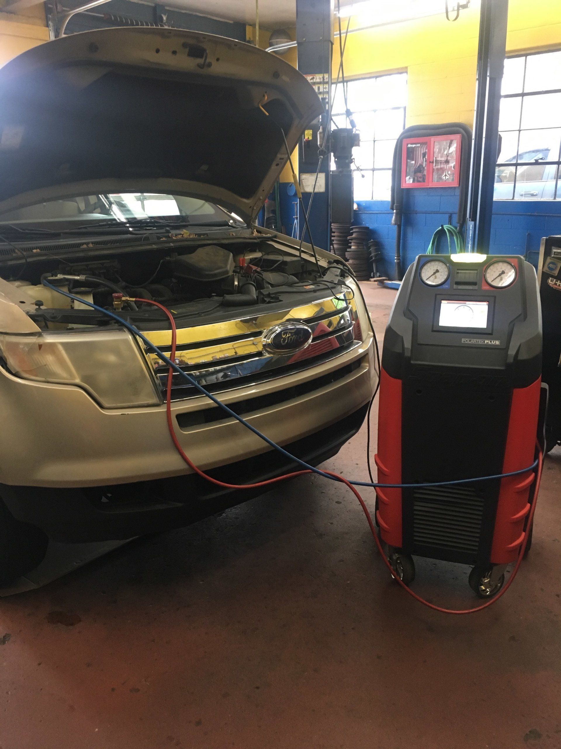 Car being serviced with an AC machine in an auto repair shop.