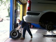 Mechanic changing a tire in a repair shop, vehicle raised. Man in blue shirt, holding the wheel.